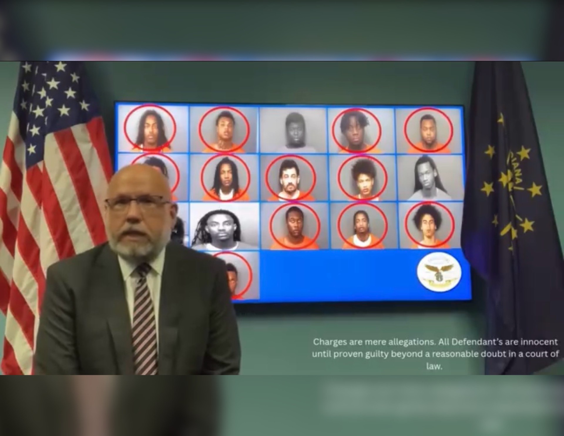 A man in a suit stands in front of a display showing mugshot-style photos of several individuals. The text below states "Charges are mere allegations. All Defendants are innocent until proven guilty beyond a reasonable doubt in a court of law.