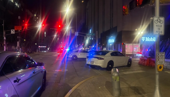 Nighttime city street with police cars, traffic, and a "Yield to Peds" sign.