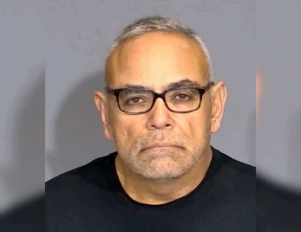 Headshot of a middle-aged man with gray hair and glasses wearing a black shirt against a gray background.