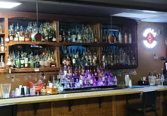 A well-stocked bar with numerous bottles, glasses, and lighting fixtures displayed on wooden shelves.