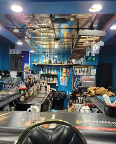 A colorful, well-stocked bar with various liquor bottles, glassware, and a chalkboard menu visible.