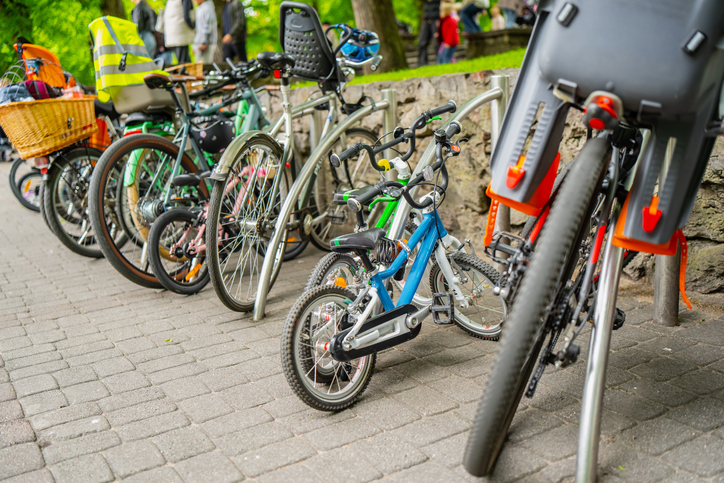 Ground level view of several standard commuter bikes and toddlers training vehicle attached to pavement security bars, safe municipal cycling transit system concept