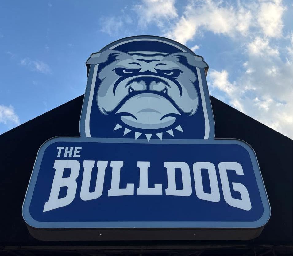 A large blue and gray logo for "The Bulldog" with a bulldog mascot against a cloudy sky.