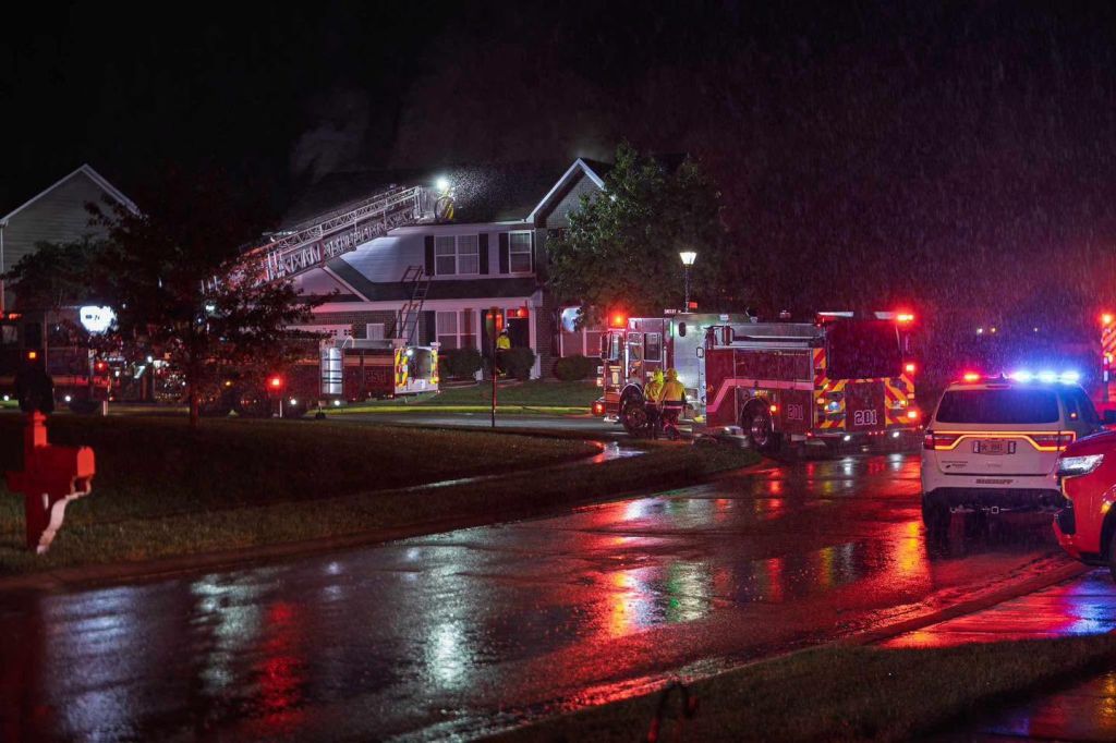 Emergency vehicles and firefighters responding to a nighttime incident at a residential house.