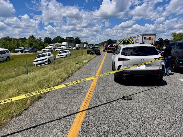 A scene of a police investigation at a roadside location, with multiple emergency vehicles and law enforcement personnel present.