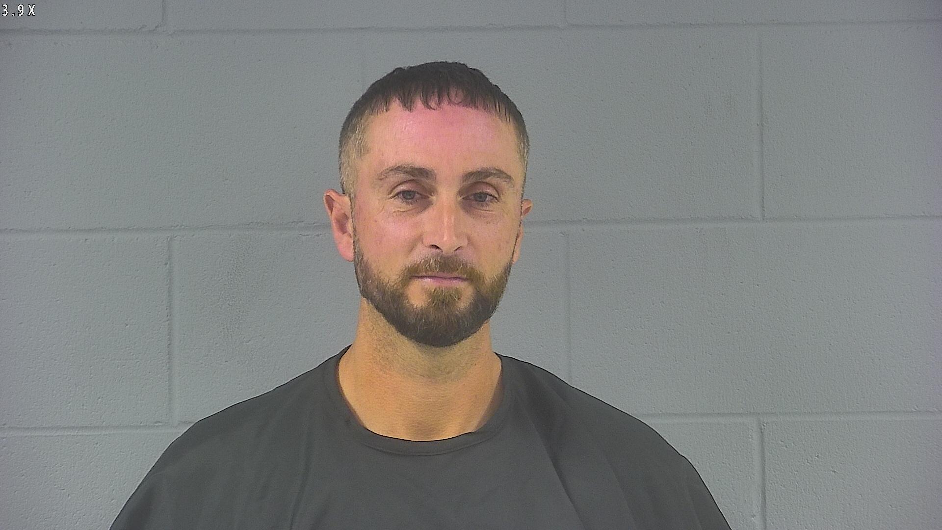 Headshot of a man with a beard wearing a black shirt against a gray wall.