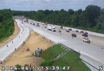 Busy highway with multiple lanes of traffic, vehicles moving in both directions, surrounded by trees and greenery.
