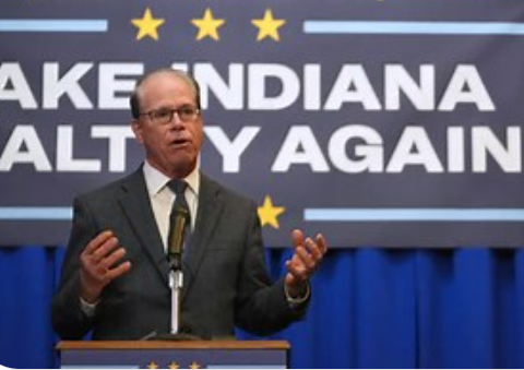 A man speaking at a podium with the text "Make Indiana Salty Again" displayed on a banner behind him.