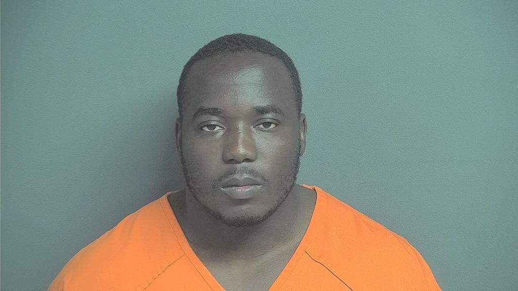 Headshot of a Black man with a serious expression, wearing an orange prison uniform.