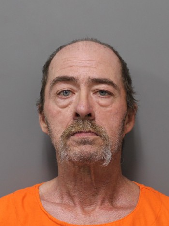 Mugshot of an older man with gray hair and a beard, wearing an orange prison uniform.