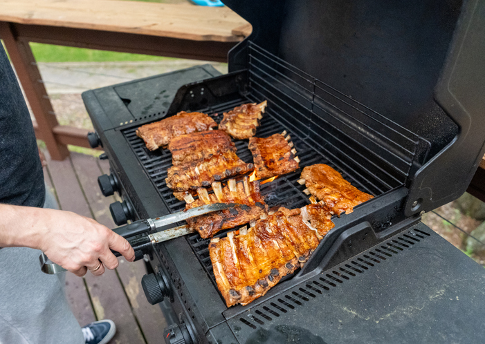 High angle view of chef turning succulent pork ribs on backyard barbecue gas grill