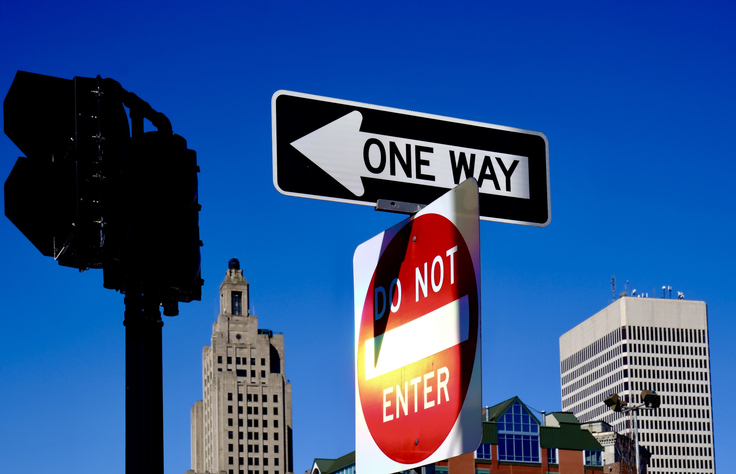 Low angle view of a One Way and Do Not Enter road signs against a clear blue sky with city buildings in the background,Providence,United States,USA
