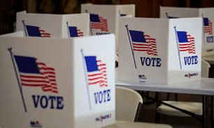 Voting booths with American flags and "VOTE" signs in a polling place.