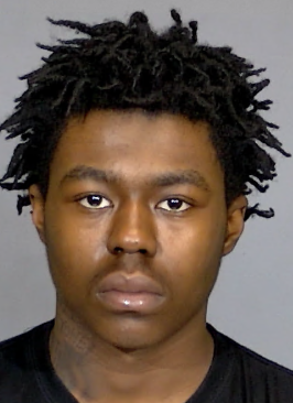 A close-up portrait of a young Black man with dreadlocked hair and a serious expression.
