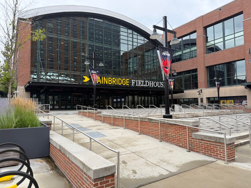 Exterior of the Ainbridge Fieldhouse, a large brick and glass sports arena with signage and steps leading to the entrance.