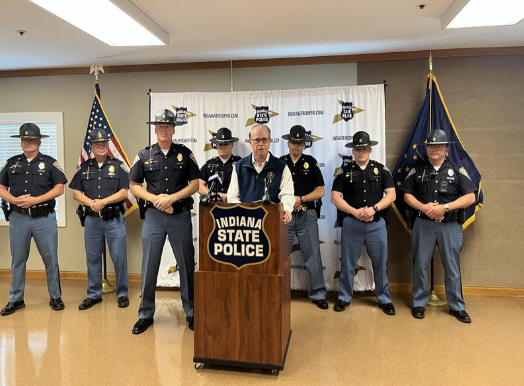 A group of Indiana State Police officers standing in front of a podium with the Indiana State Police logo.
