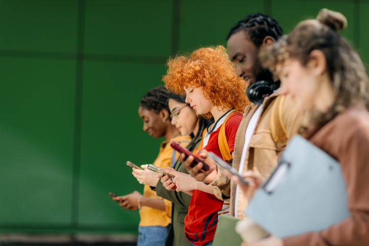 Diverse university students using smartphones outside campus building
