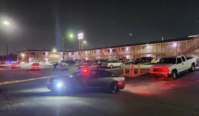 Nighttime parking lot with several vehicles, including a police car with flashing lights.