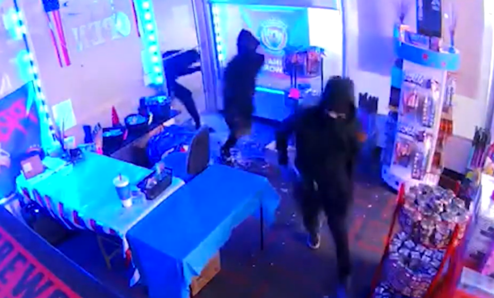 Two people in dark clothing entering a room with various electronic equipment and lighting.