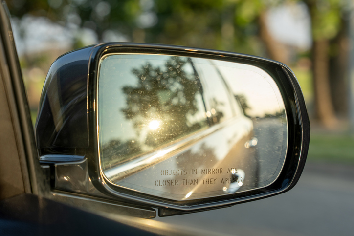 Reflection of golden hour sun in a car side-view mirror with safety warning text