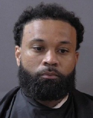 A man with a beard wearing a black shirt looks directly at the camera.