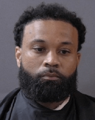 A man with a beard wearing a black shirt looks directly at the camera.