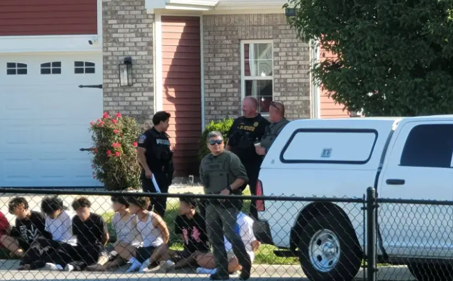 Several people, including police officers, standing outside a residential building with a pickup truck parked nearby.