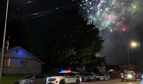 Nighttime scene with police cars and fireworks in the sky above a residential neighborhood.