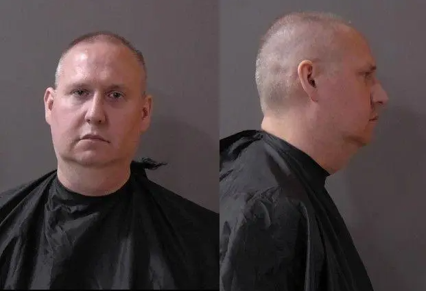 Headshot of a middle-aged man with a serious expression, wearing a black jacket.