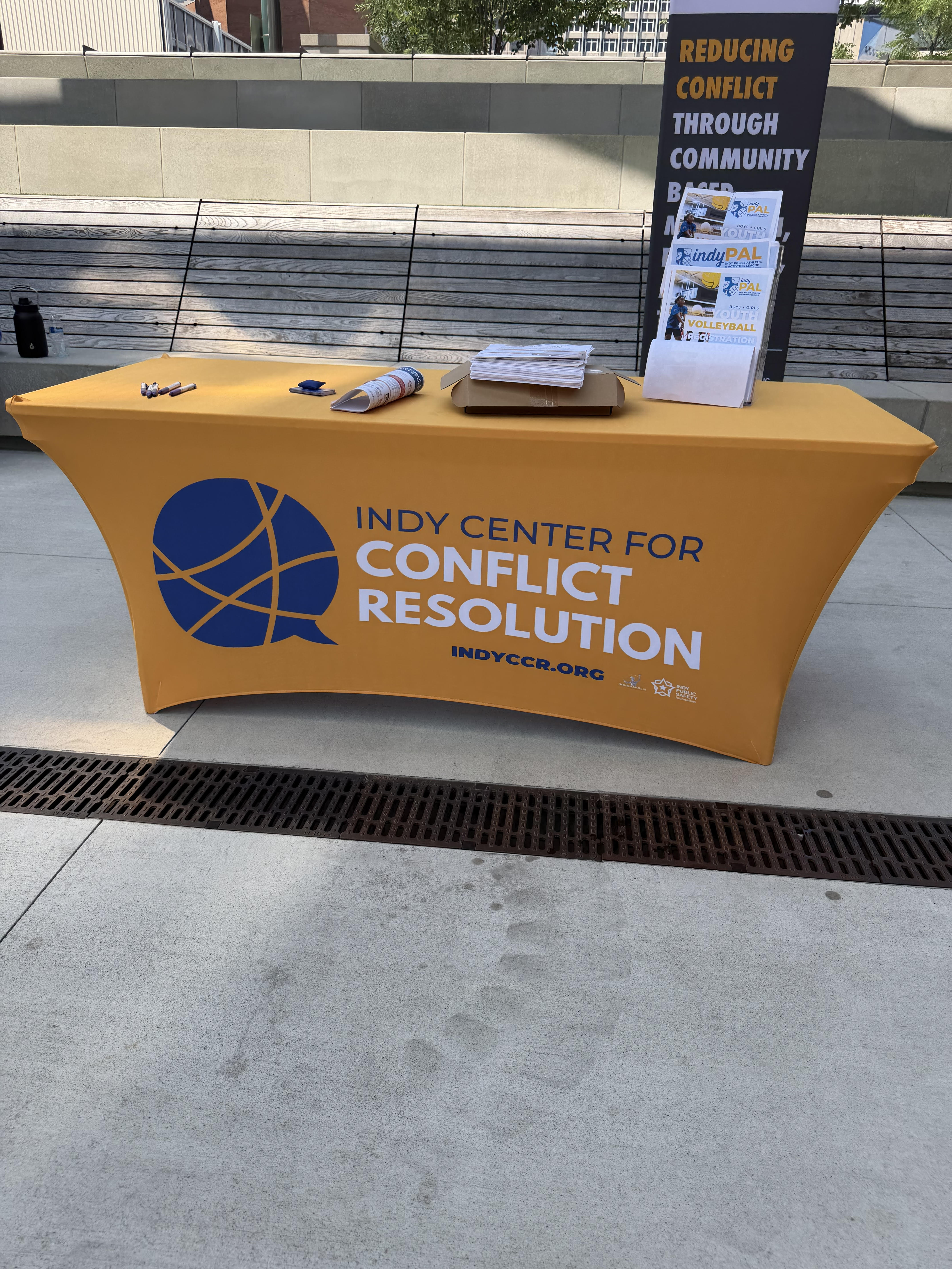 A yellow table with the Indy Center for Conflict Resolution logo and text promoting community-based conflict resolution programs.