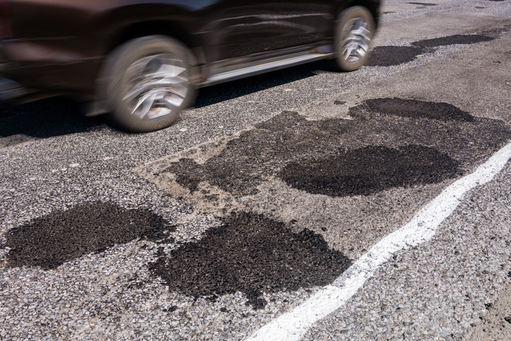 Car Driving on Road After Pothole Repair, Multiple Asphalt Patches, Poor Pavement Condition and Vehicle Damage Risk