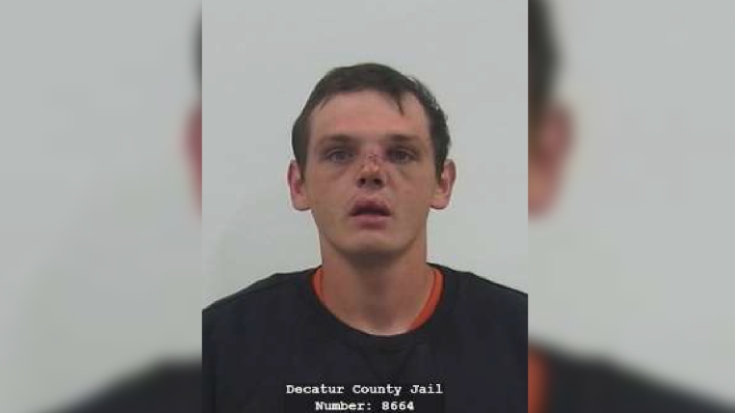 Mugshot of a man with short dark hair wearing a black shirt and looking directly at the camera.