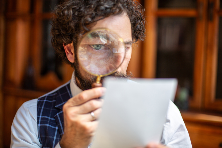 Man closely examining text on a paper using a magnifying glass