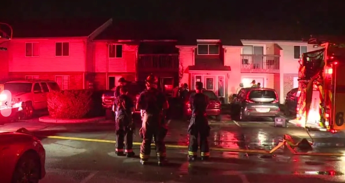 Emergency vehicles and personnel responding to an incident at night in a residential area, with buildings illuminated in red light.
