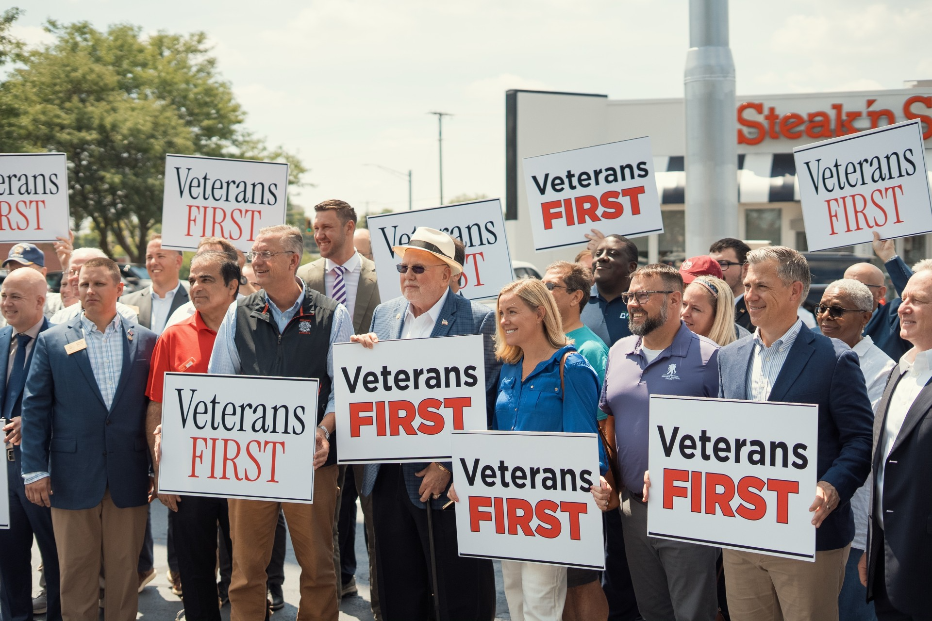 A group of people holding "Veterans First" signs at a rally or protest.