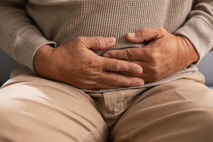 Suffering asian elder in need of medical care feels severe stomach pain clutching abdomen with hands showing deep discomfort