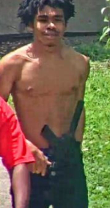 Shirtless man standing in a grassy outdoor setting.