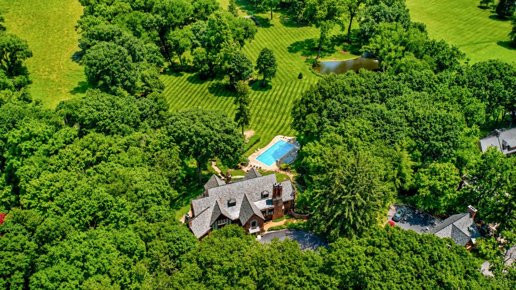 Aerial view of a large, wooded estate with a swimming pool, manicured lawns, and a stately manor house.
