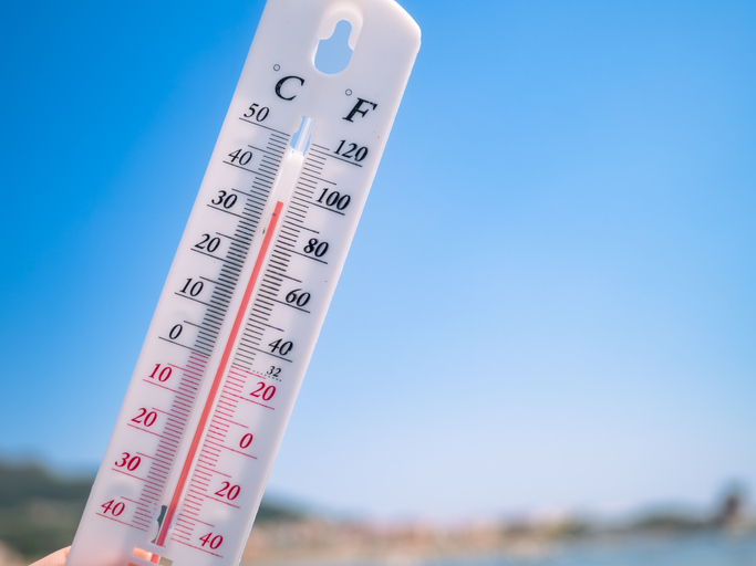 Close-up of thermometer showing high summer temperature against blue sky