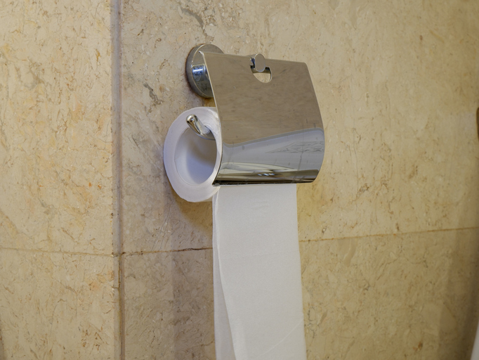 Toilet paper roll on chrome metal holder mounted on a beige marble tile wall in a modern bathroom restroom interior closeup
