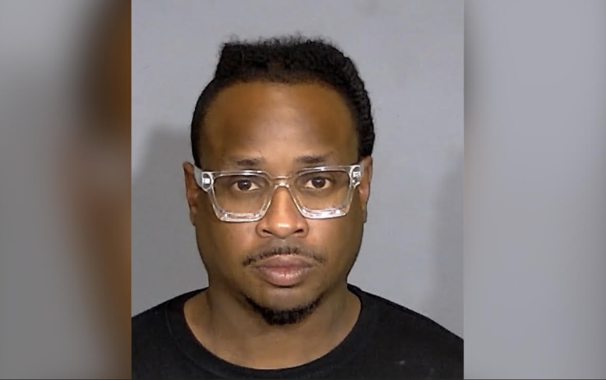 A headshot of a man wearing glasses and a black shirt against a gray background.