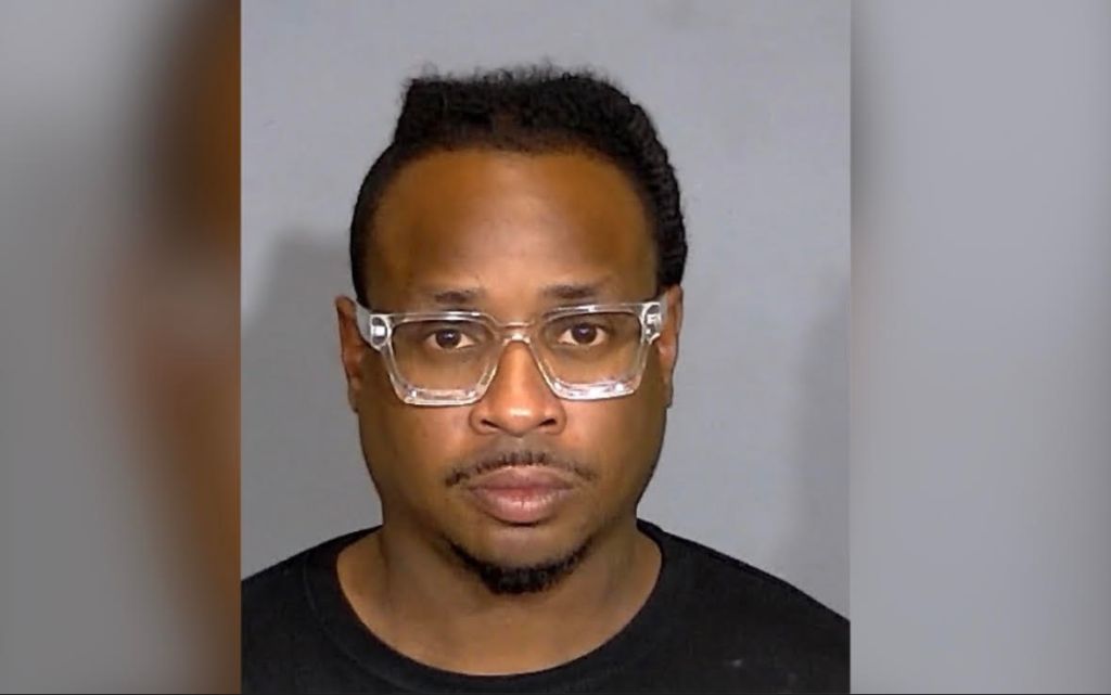 A headshot of a man wearing glasses and a black shirt against a gray background.