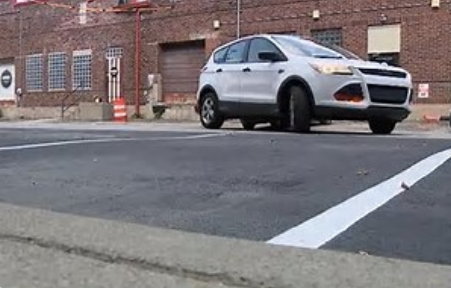 A white Ford SUV parked on a city street with a crosswalk and buildings in the background.