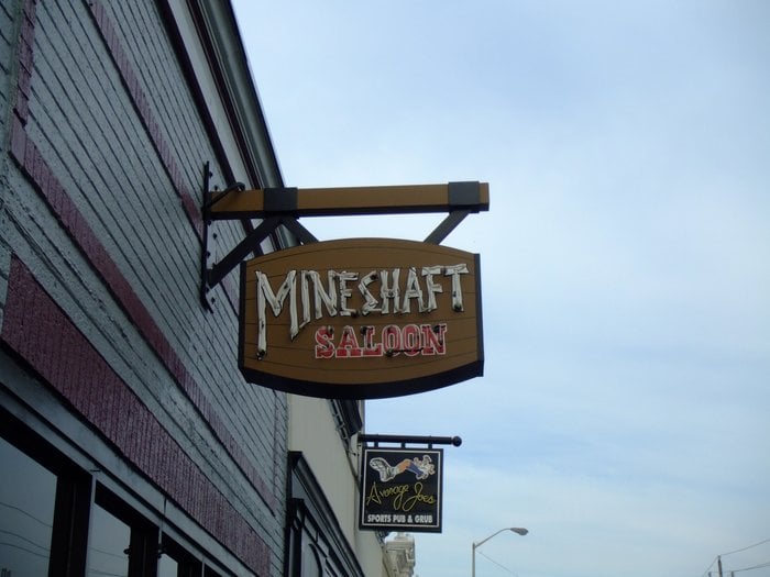 A wooden sign hanging on a building that reads "Mineshaft Saloon".