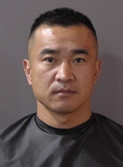 Headshot of a serious-looking Asian man with short dark hair wearing a black shirt against a gray background.