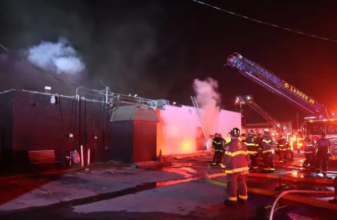 Firefighters battling a blaze at night, with smoke and flames visible from a structure fire.