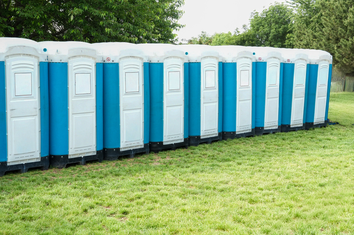 Row of blue and white public toilets on a grassy lawn. Bio toilets at a concert