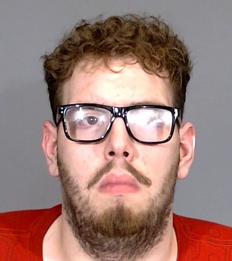 A man with curly hair and a beard wearing black-framed glasses and a red shirt.