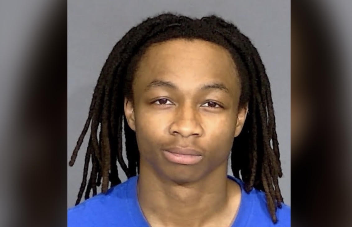 Headshot of a young Black man with dreadlocks wearing a blue shirt against a gray background.