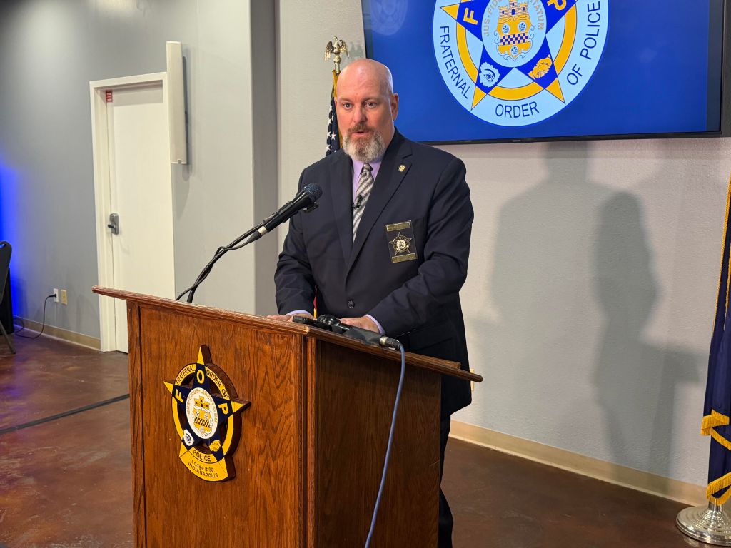 A man in a suit and tie standing at a podium with the logo of the Fraternal Order of Police displayed behind him.